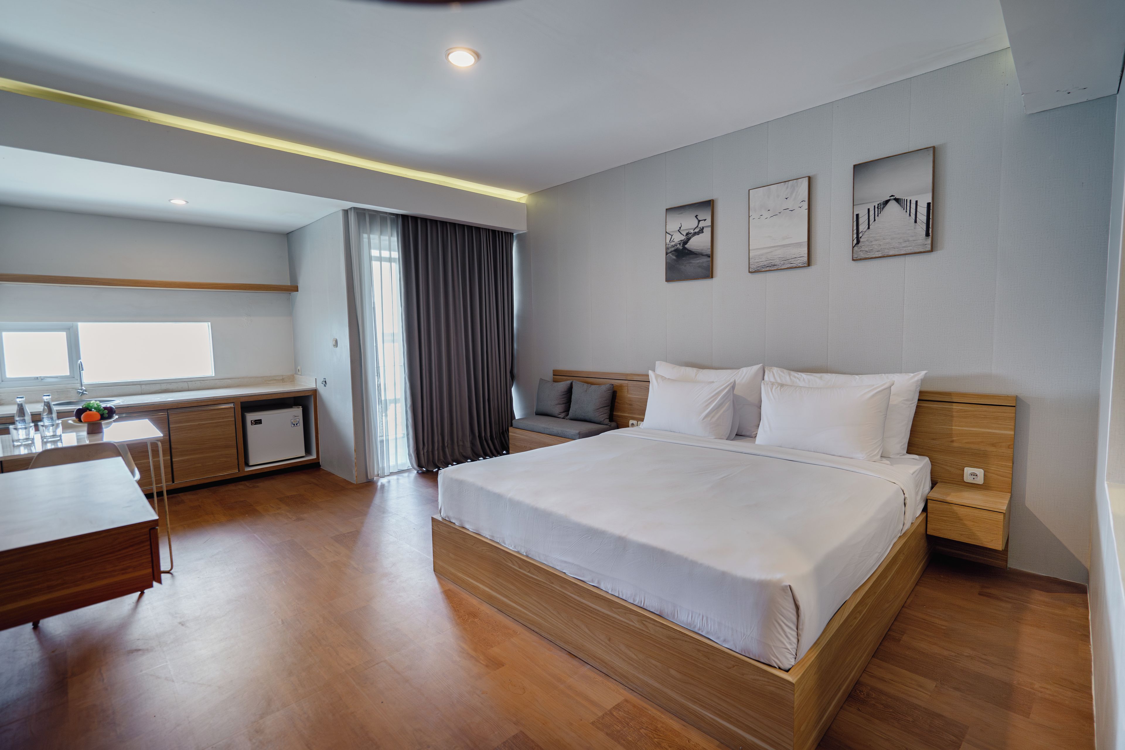 A modern hotel room with a large bed, a desk, a small kitchenette, and a view of the outdoors.