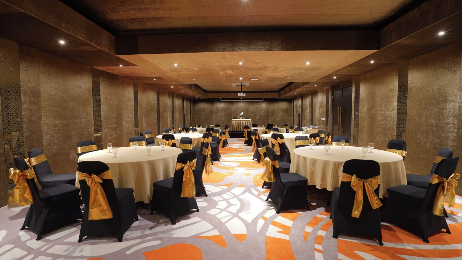 A banquet hall with round tables and chairs, each with a gold sashed chair.