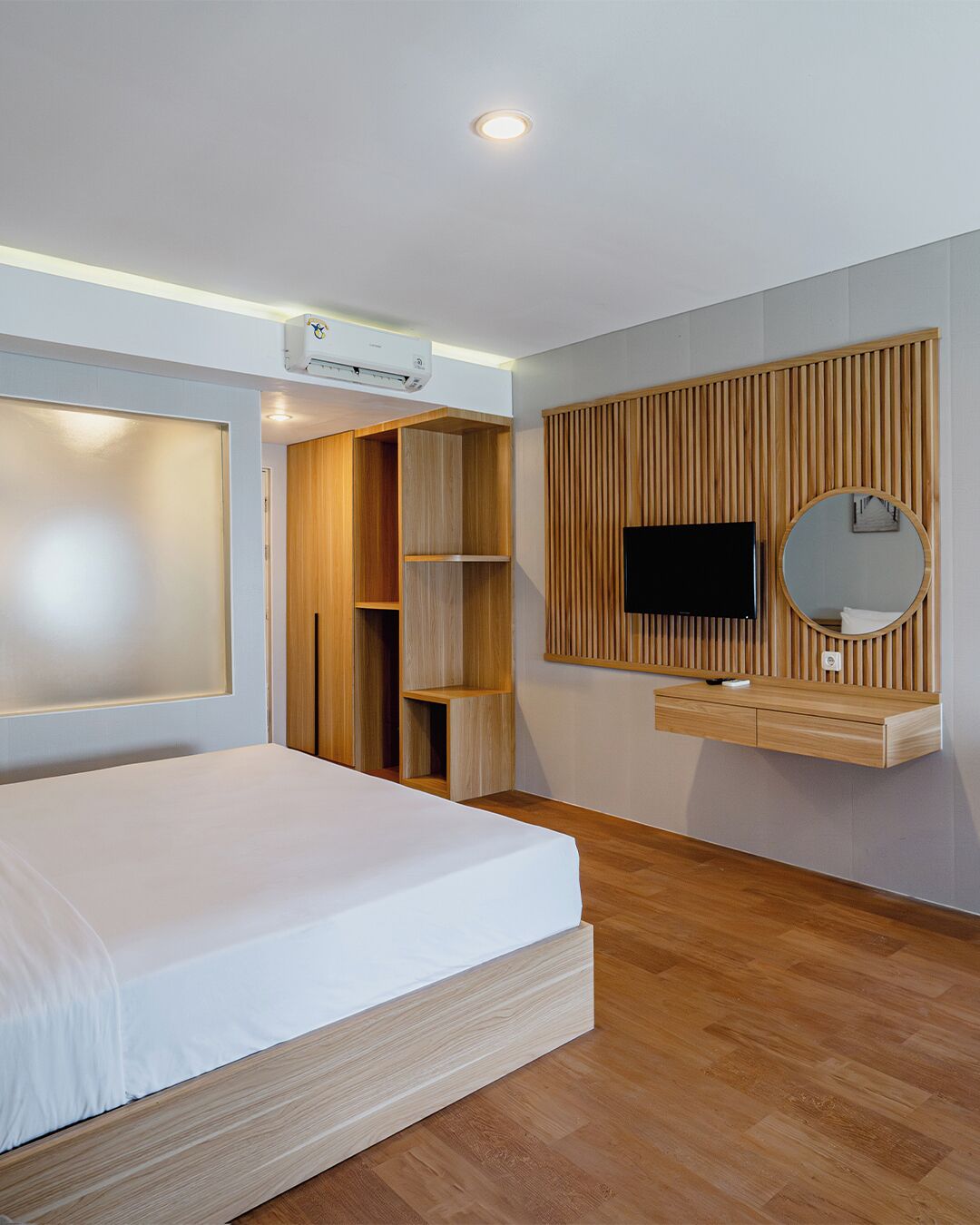 Un dormitorio moderno con cama, estanterías empotradas de madera, televisor montado y equipo de aire acondicionado.