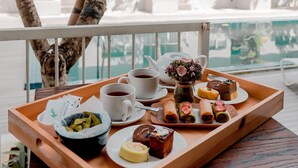 A tray with food and drinks on a table by a poolside, with a view of a building and trees in the background.