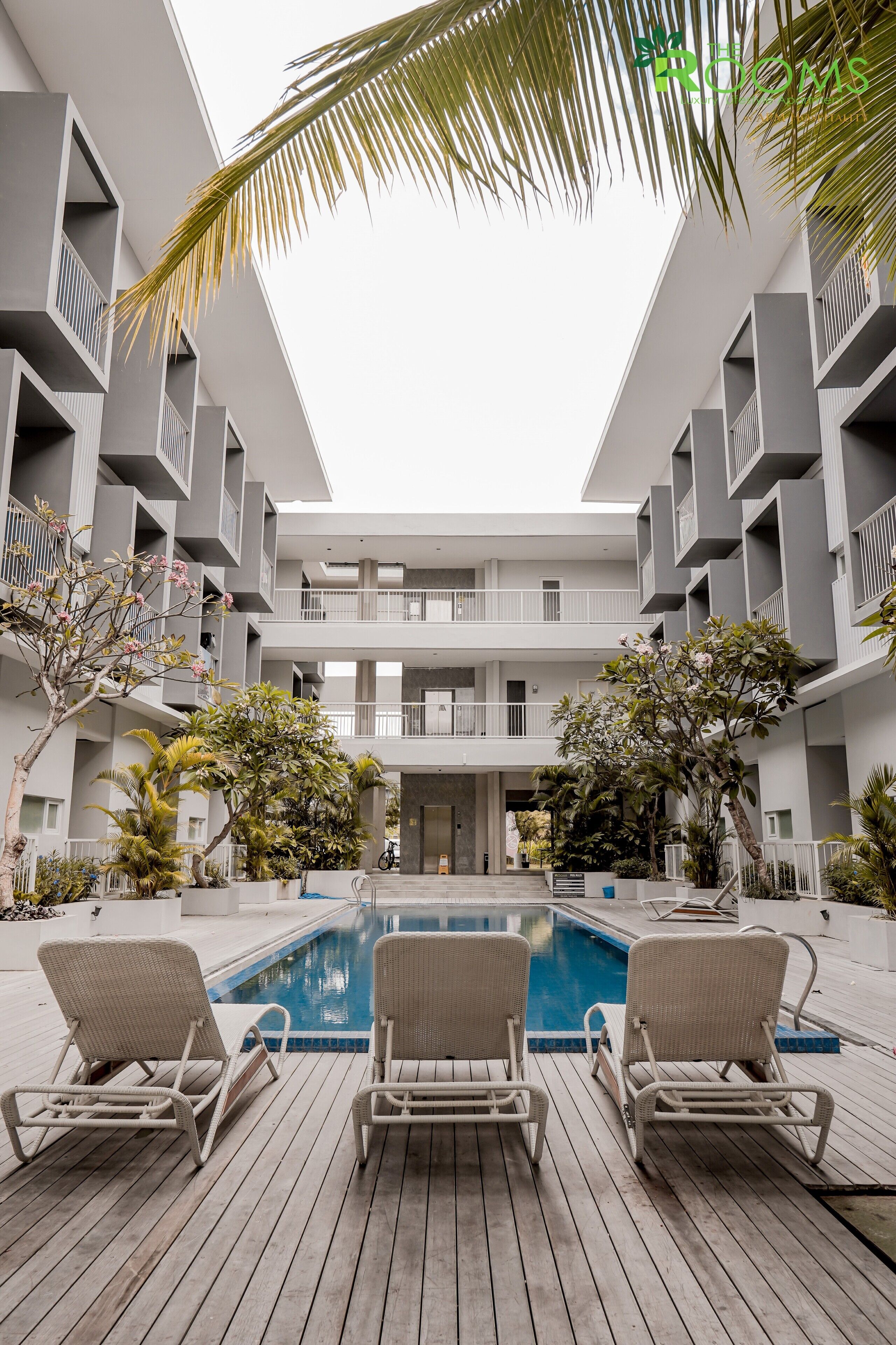 A modern building with a central pool, surrounded by lounge chairs and greenery.