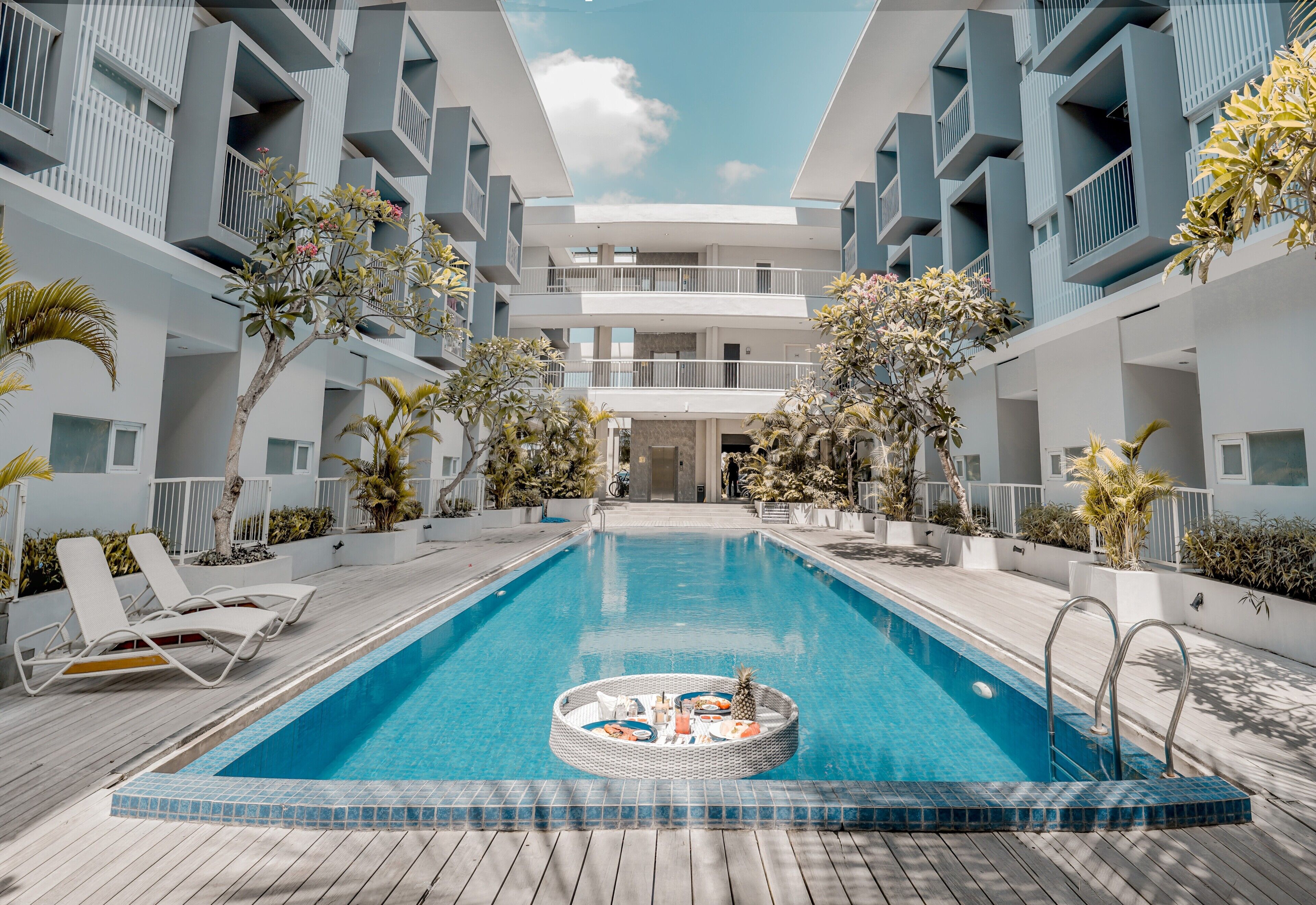 A modern hotel pool area with a clear blue pool, lounge chairs, and potted plants.