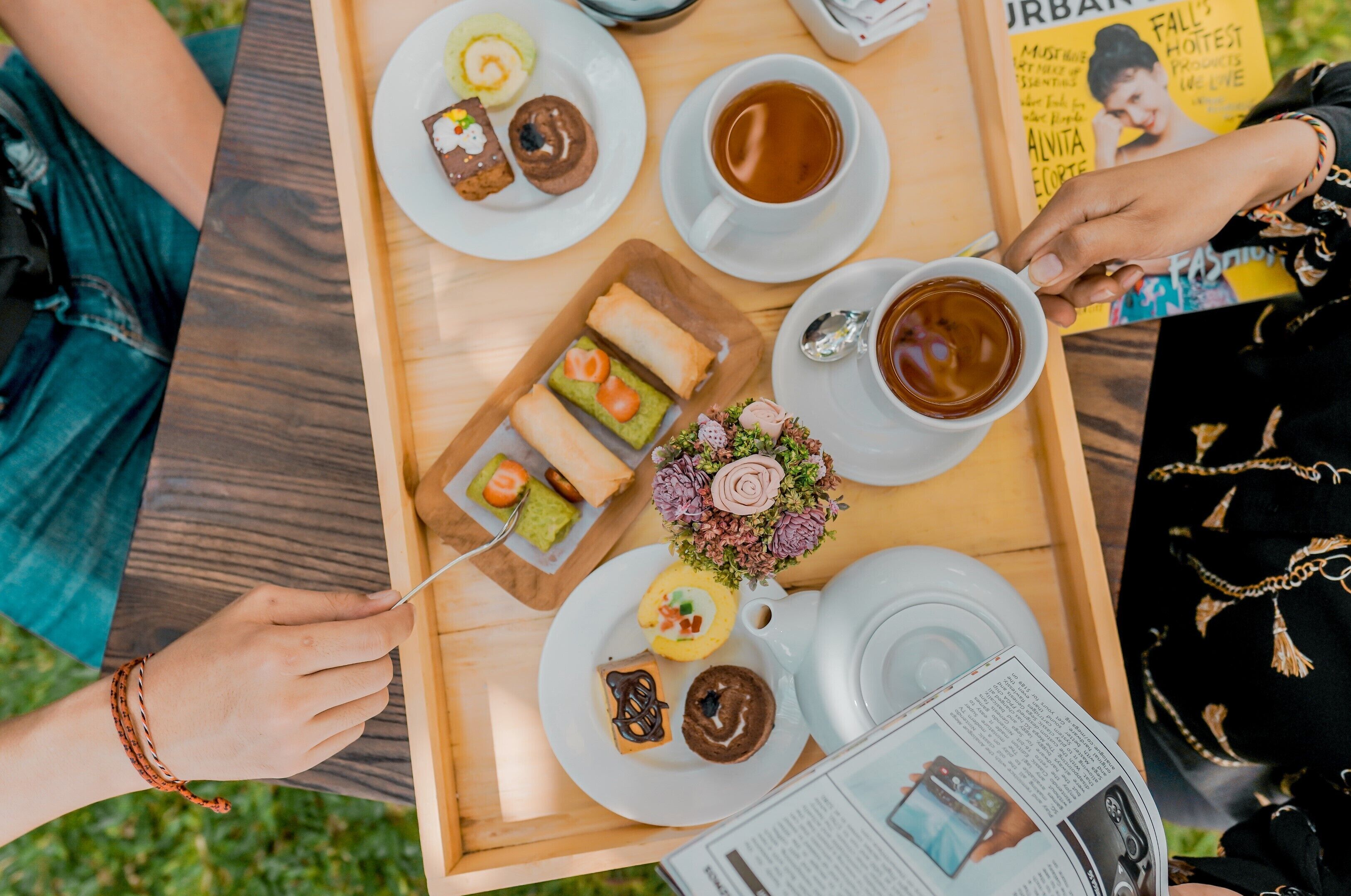 A wooden tray with various pastries, a cup of tea, and a small flower arrangement.