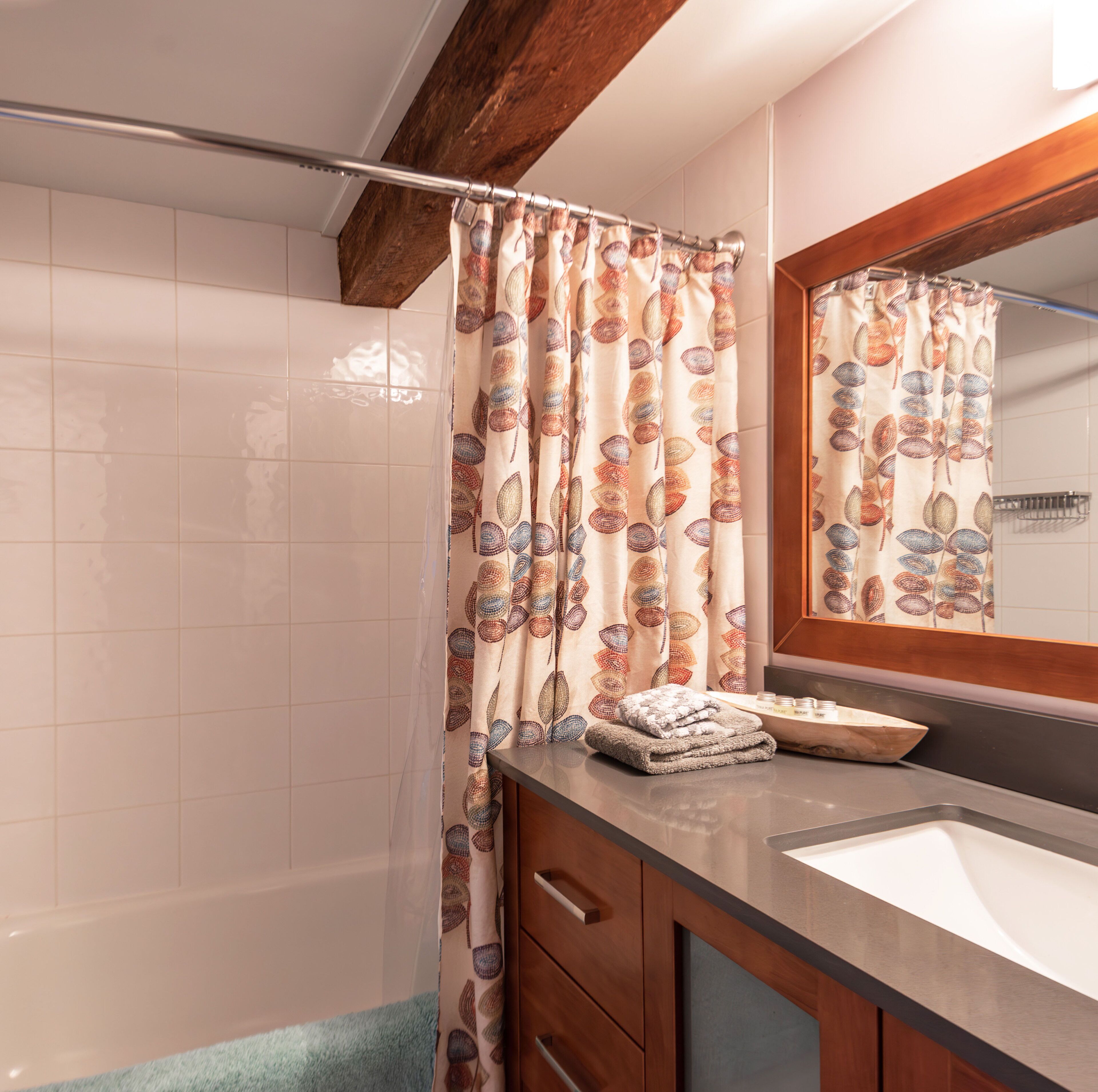 A bathroom with a shower curtain featuring a leaf pattern, a wooden vanity with a sink, and a mirror above the sink.