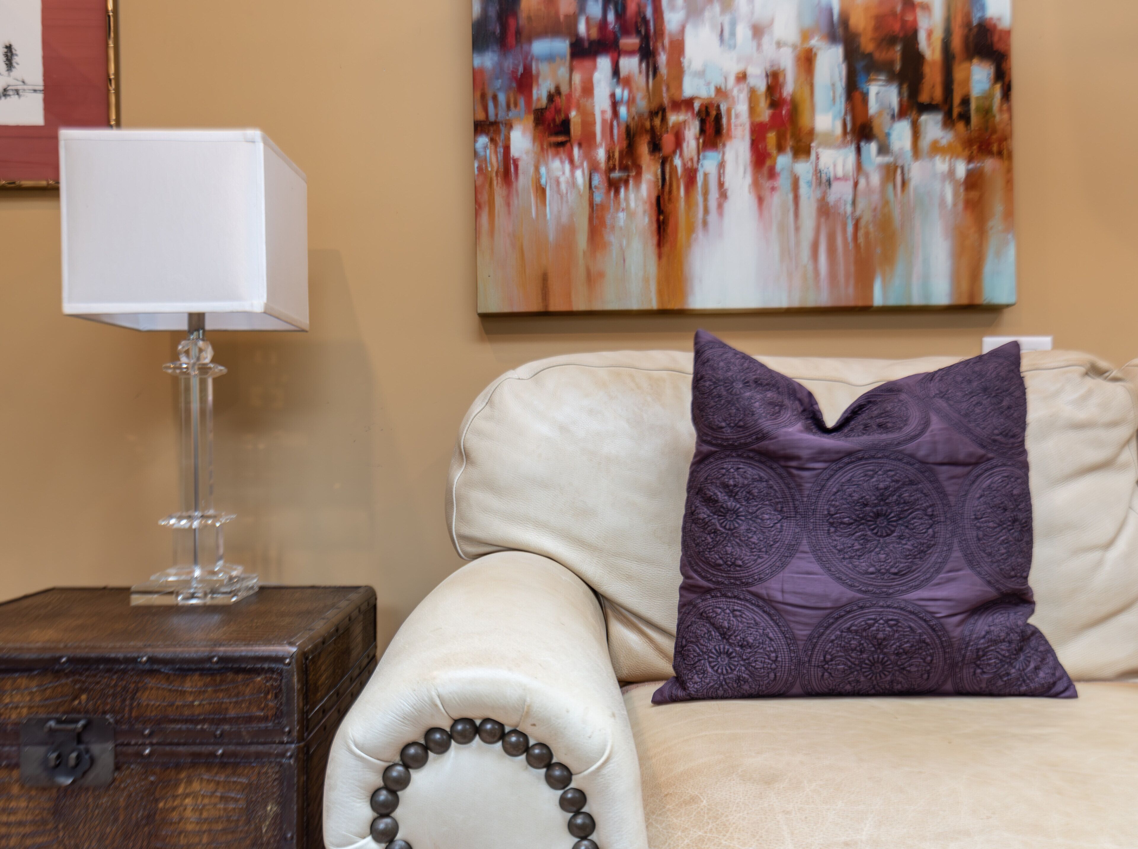 Un sofá beige con un cojín decorativo y una lámpara de cristal sobre una mesita de madera.