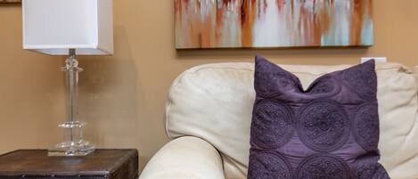 A beige sofa with a decorative pillow and a clear glass lamp on a wooden side table.