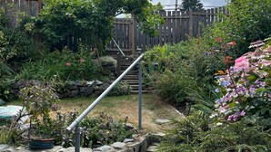 Een tuin met een stenen trap, een houten omheining en diverse planten en bloemen.