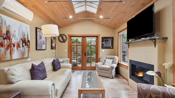 Een woonkamer met houten plafond, een open haard, een bank, een fauteuil en een televisie.