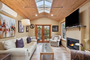 A living room with a wooden ceiling, a fireplace, a sofa, a chair, and a television. - Spacious character suite! Close to local private schools, dining and more! (Shawnigan Lake)