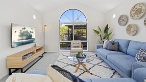 Ein modernes Wohnzimmer mit einem großen, bogenförmigen Fenster, einem blauen Sofa, einem Couchtisch und einem Flachbildfernseher auf einem Holzständer.