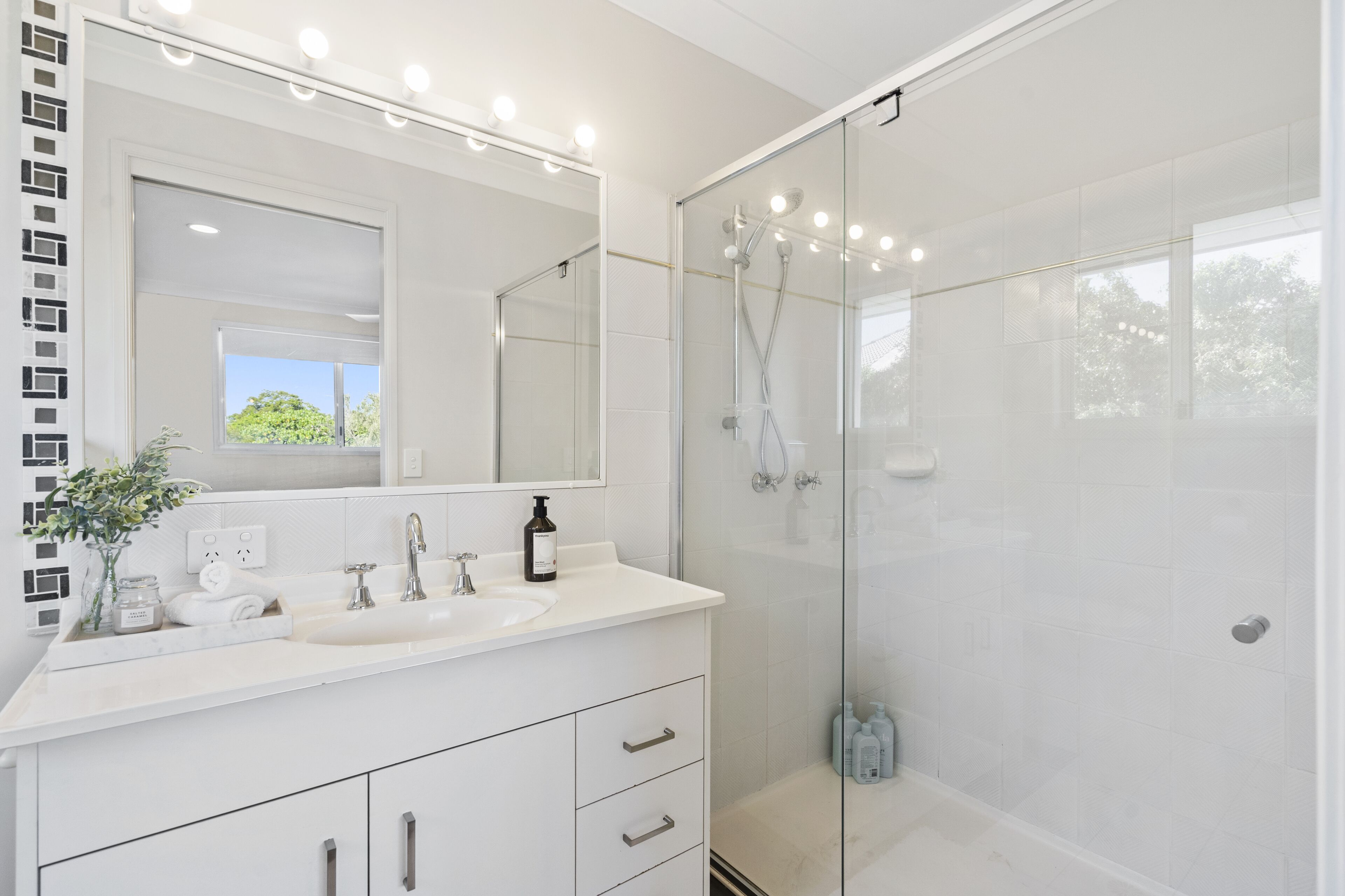 A modern bathroom with a glass-enclosed shower, a white vanity with a sink, and a large mirror with lights.