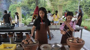 Un groupe de personnes prépare des aliments à l’extérieur, sur une table où sont disposés des pots en terre cuite et des ustensiles de cuisine.