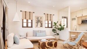 A modern living room with a sofa, a wooden coffee table, a wicker chair, and a large plant. - Beach Club Included | 1 min to beach | sleeps 5 | Plaza Mercado 12 (Las Catalinas)