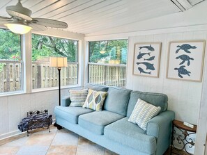 A light blue sofa with patterned cushions, a ceiling fan, and framed artwork on the wall. - The Floridian, 5 beds, Sleeps 7, Ping Pong Table (Mount Dora)