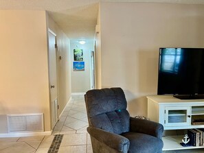 Una sala de estar con televisor, un sillón gris y un mueble blanco para entretenimiento.