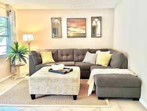 A living room with a grey sofa, a patterned ottoman, and a coffee table with a tray. There are three framed pictures on the wall. - The Floridian, 5 beds, Sleeps 7, Ping Pong Table (Mount Dora)