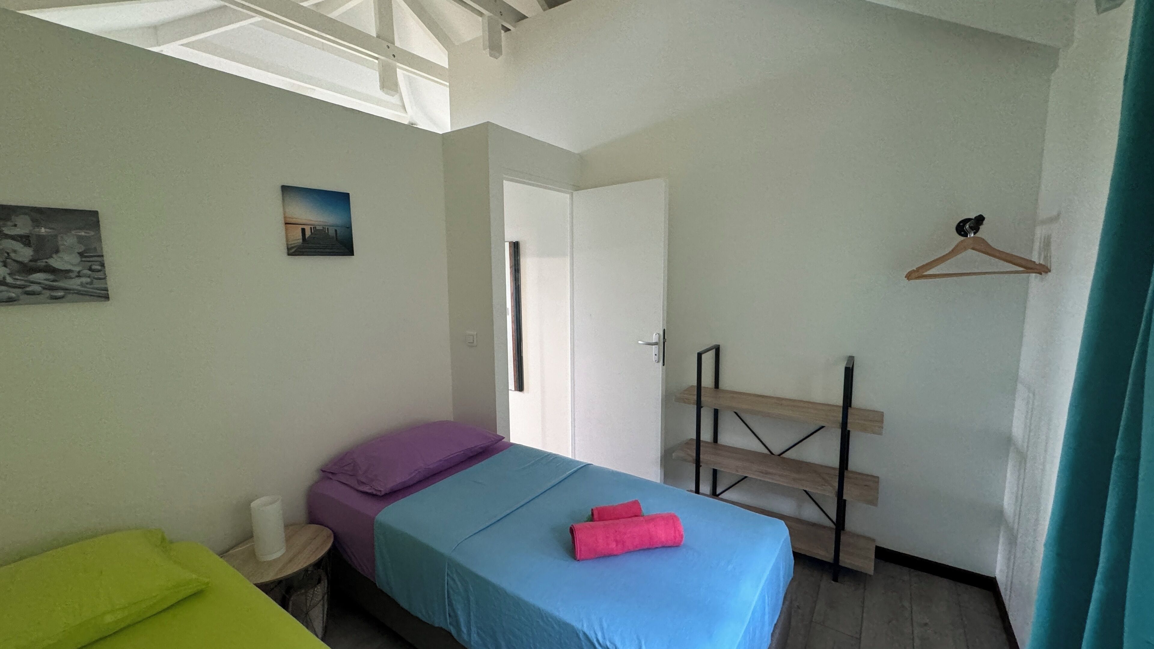 A bedroom with a bed, a small table, a hanging light, and a door.