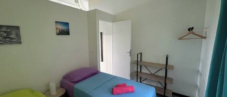 A bedroom with a bed, a small table, a hanging light, and a door.