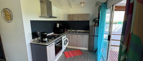 A modern kitchen with a built-in oven, microwave, and coffee maker. There is a washing machine and a sink. The kitchen has wooden cabinets and a red rug.