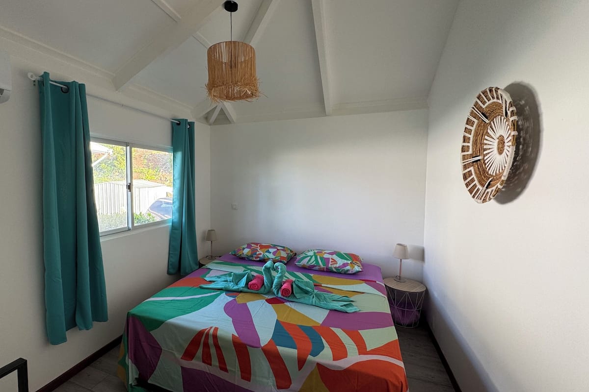 A bedroom with a bed, teal curtains, a window, a wall clock, and a ceiling fan.