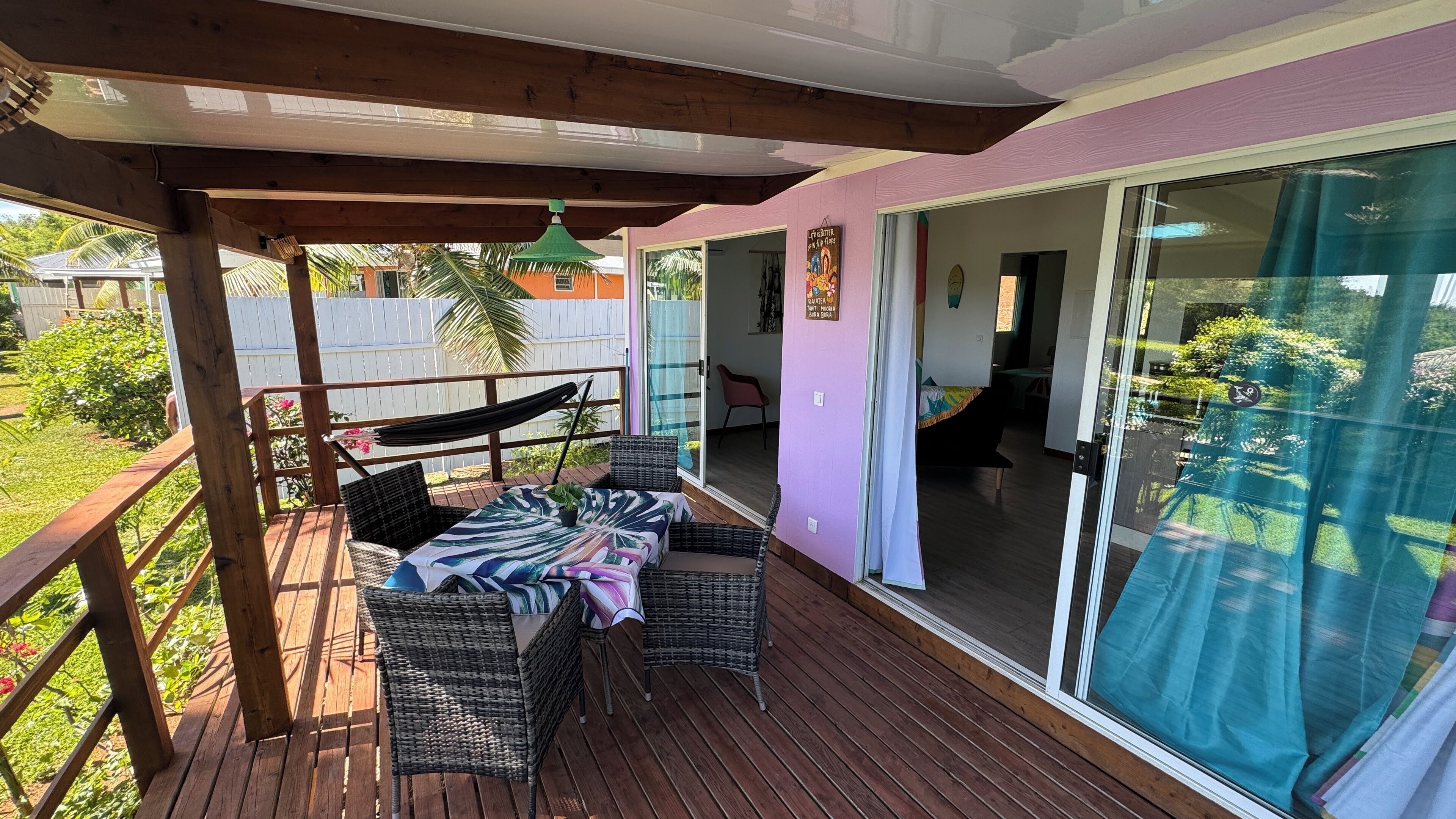 Eine überdachte Terrasse mit Korbmöbeln, einer Hängematte und Blick auf den Garten.