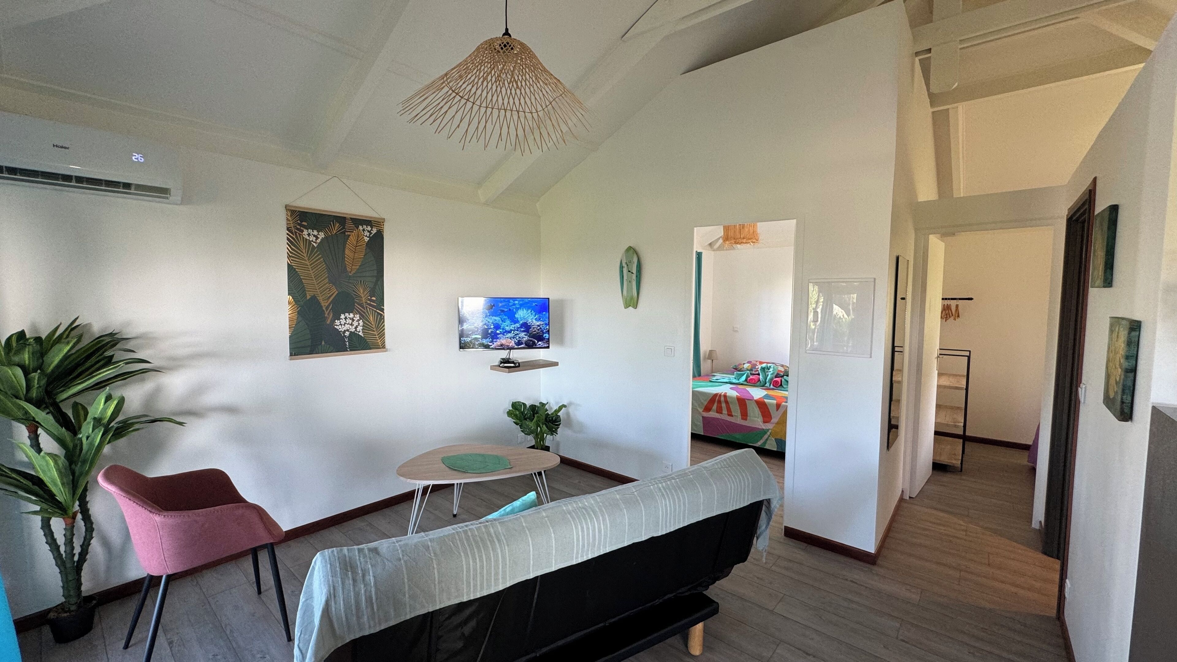 A modern living room with a sofa, a small table, a TV, and a hanging light fixture.