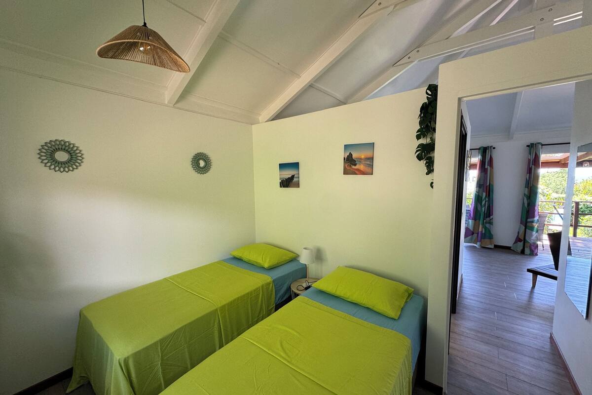 A room with two single beds, a hanging light fixture, and a view of the outdoors.