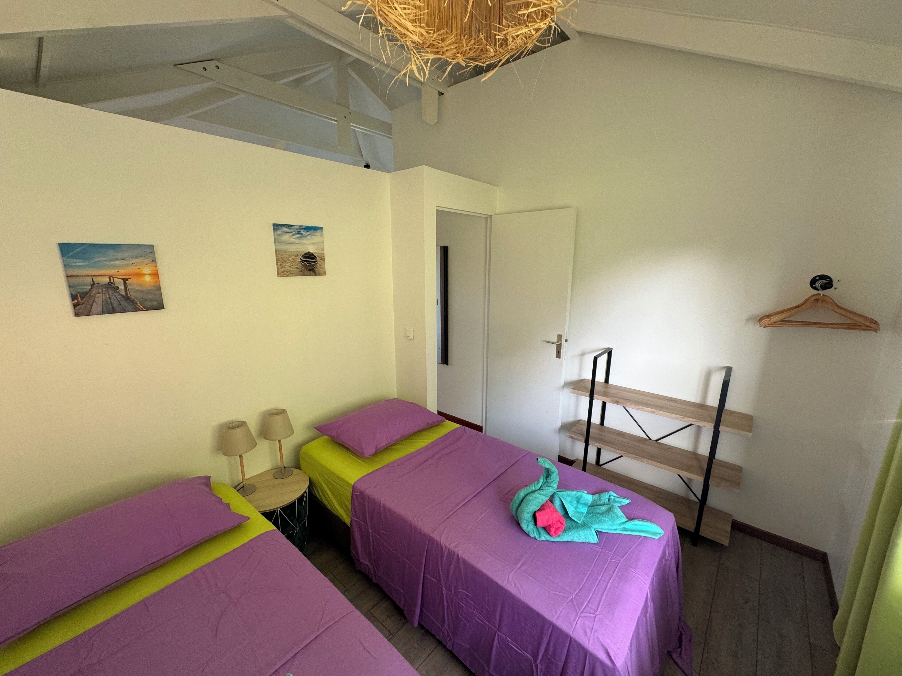 A room with two beds, a small table, a lamp, and a wooden hanger rack.