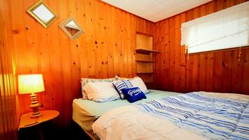 A wooden-paneled room with a bed, a bedside table with a lamp, and two wall mirrors.