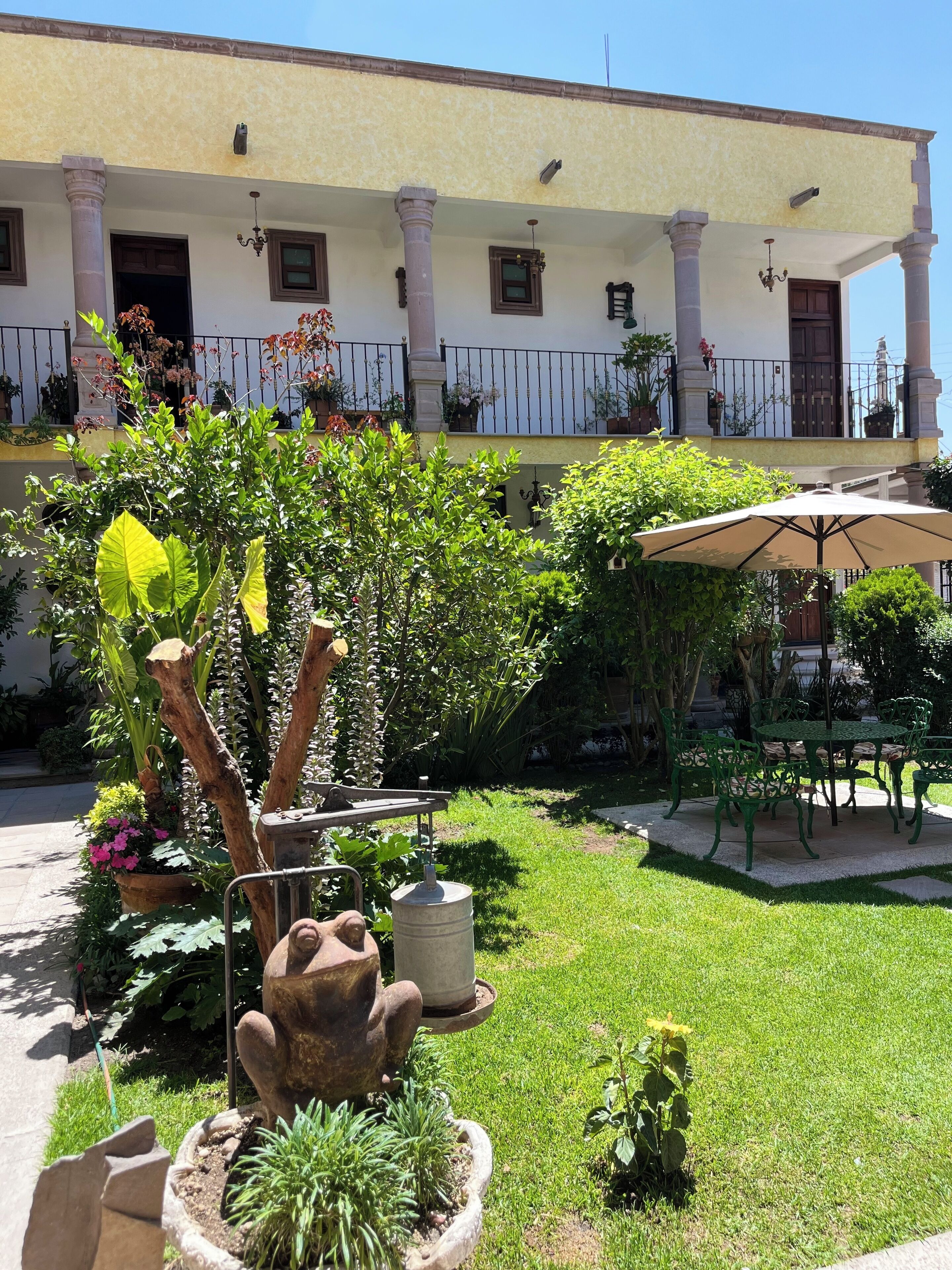 A courtyard with a dining area, potted plants, and a building with columns and balconies.