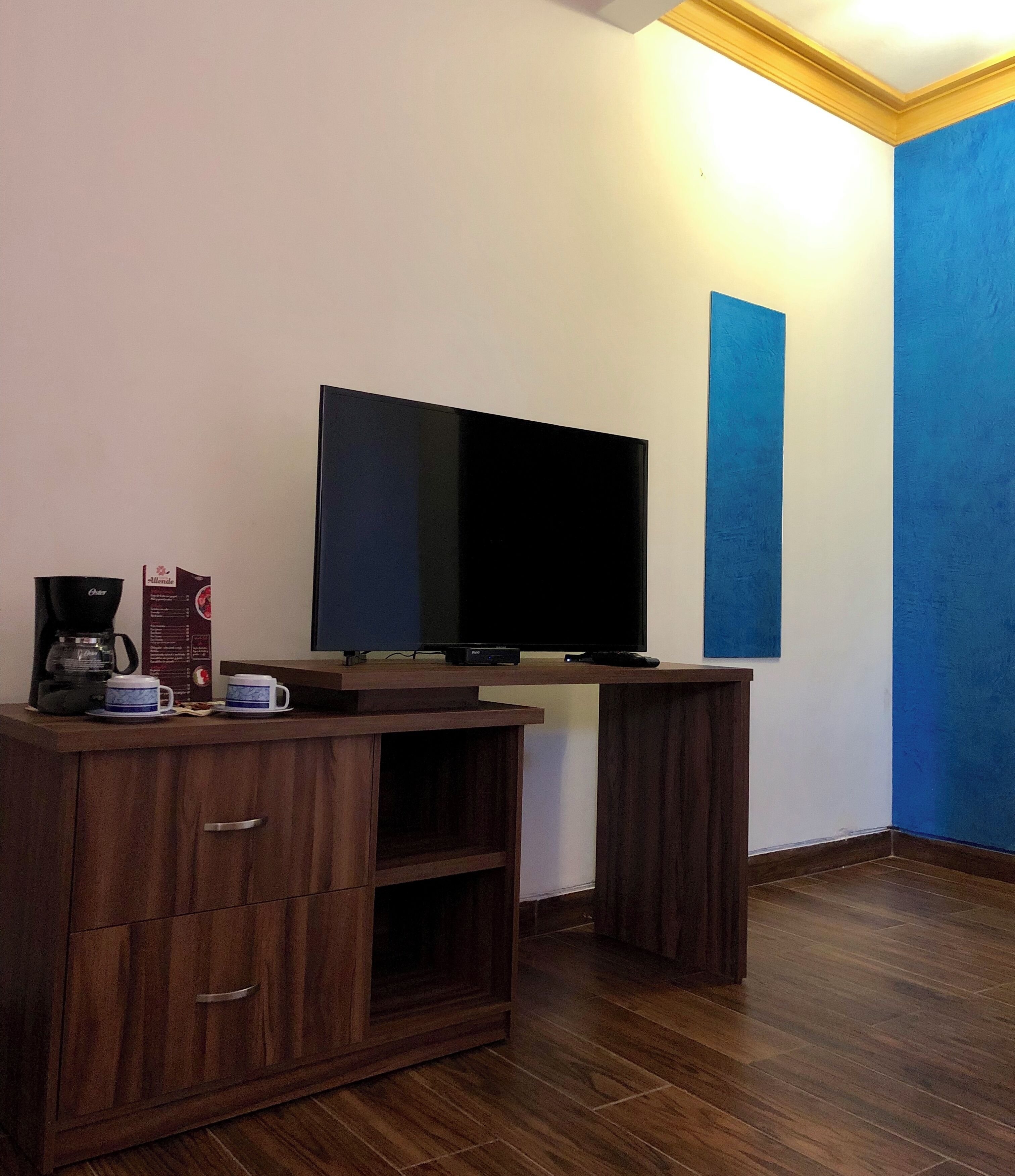 A room with a flat-screen TV on a stand, wooden furniture, and a coffee maker.