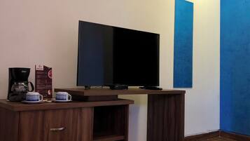 A room with a flat-screen TV on a stand, wooden furniture, and a coffee maker.