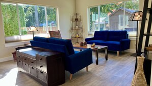 Un salon spacieux avec deux canapés bleus, une table basse en bois et un meuble en bois foncé. De grandes fenêtres offrent une vue sur l’extérieur.