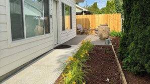 Une maison avec un porche couvert, une clôture en bois et un jardin où poussent des fleurs jaunes.