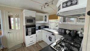 Une cuisine compacte avec des meubles blancs, un four encastré, un four à micro-ondes, une cuisinière à gaz et un lave-linge.