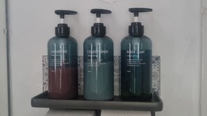A bathroom shelf with three bottles of shampoo, conditioner, and body soap.