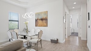 Ein moderner Essbereich mit einem Glastisch, weißen Stühlen und einem Gemälde an der Wand.