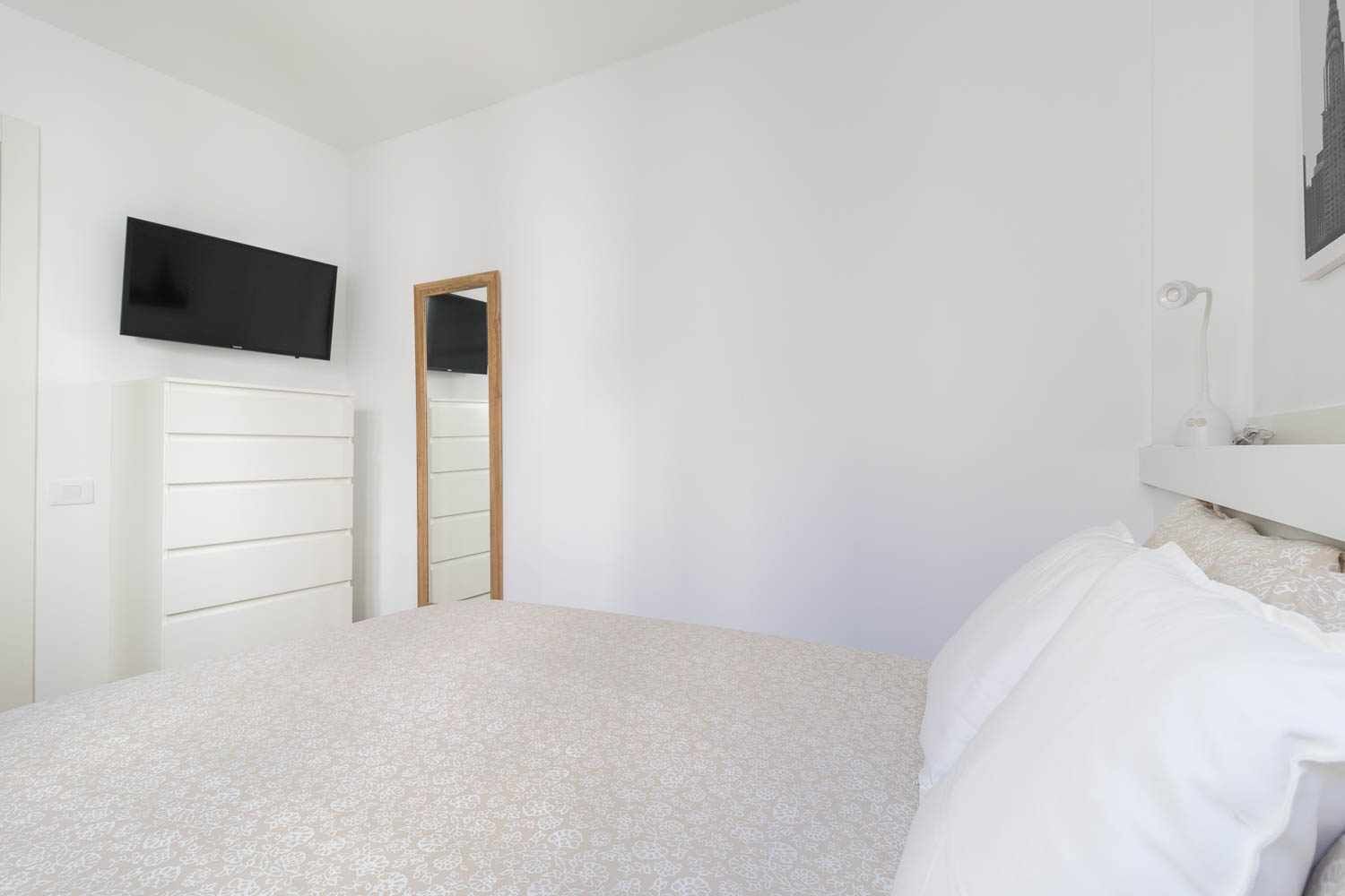 A bedroom with a bed, a dresser, a television mounted on the wall, and a mirror.