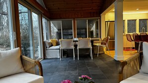 Una habitación amplia con techo de madera, ventanas grandes, zona de comedor con mesa y sillas, y área de estar con sofás y sillones.