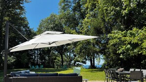 Un patio al aire libre con un paraguas grande, mobiliario de mimbre y vista al mar.