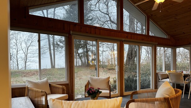 Una habitación amplia con ventanas grandes, mobiliario de mimbre y vista a árboles.