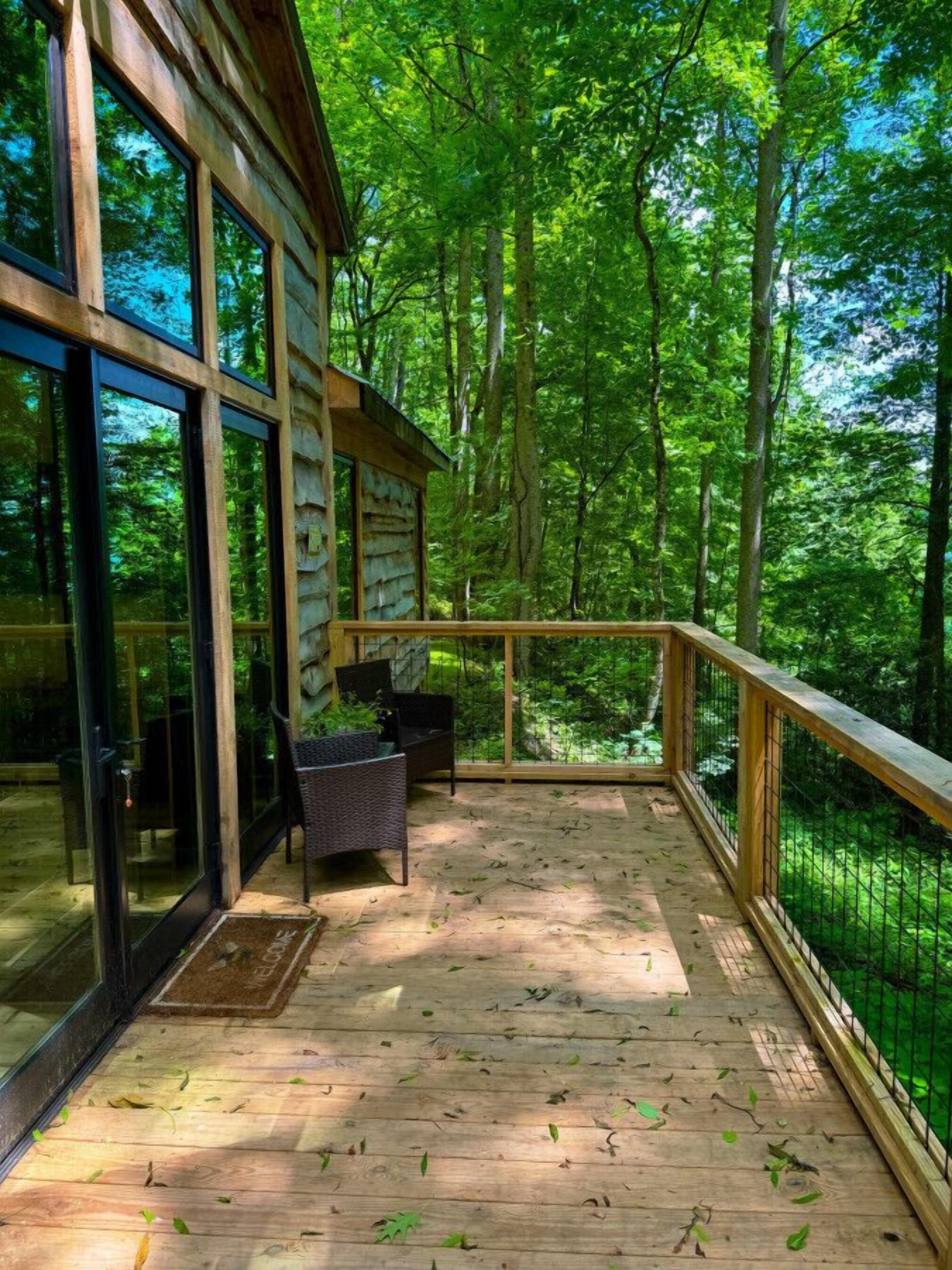 Una terraza de madera con puertas de cristal que dan a una habitación, rodeada de bosque.