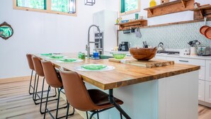 A modern kitchen with a wooden island, white cabinets, and a herringbone backsplash.