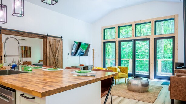 A modern kitchen with a wooden island, large windows, and a dining area with yellow chairs.