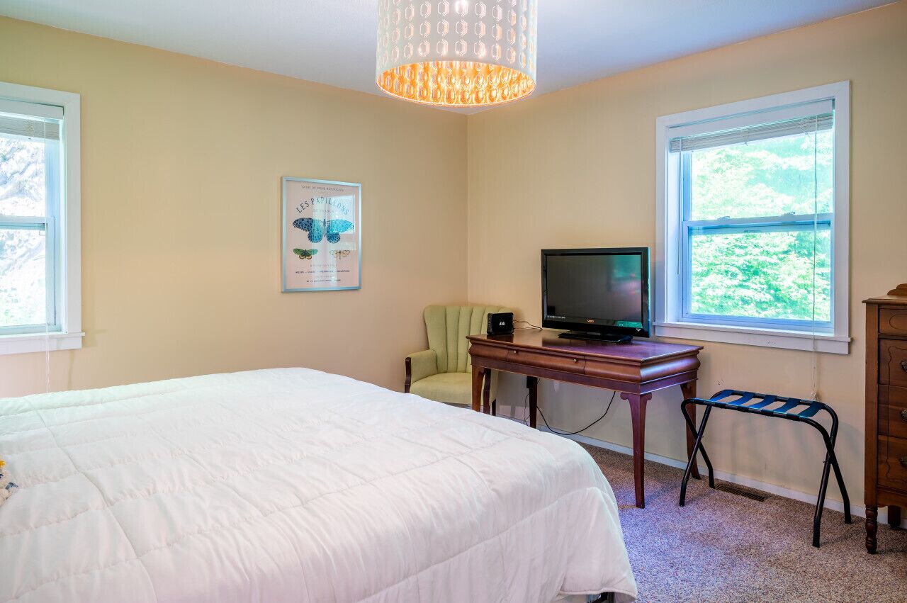 A bedroom with a bed, a desk with a television, a chair, and a window.