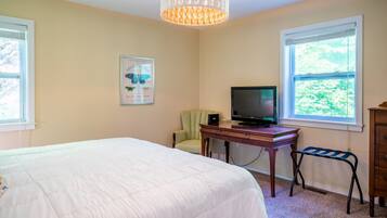 A bedroom with a bed, a desk with a television, a chair, and a window.
