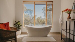 Ein modernes Badezimmer mit freistehender Badewanne, einem großen Fenster und Blick auf Bäume.
