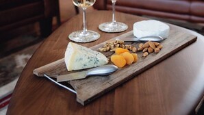 Ein Holztisch mit einer Käseplatte, zwei Gläsern Weißwein und einer braunen Ledercouch im Hintergrund.