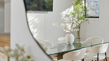 A modern dining area with a glass table, white chairs, and a vase of white flowers.
