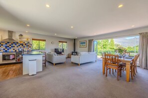 A modern living room with a kitchen, a dining area, and a balcony with a view. - Terrific views on Totara (Wānaka)